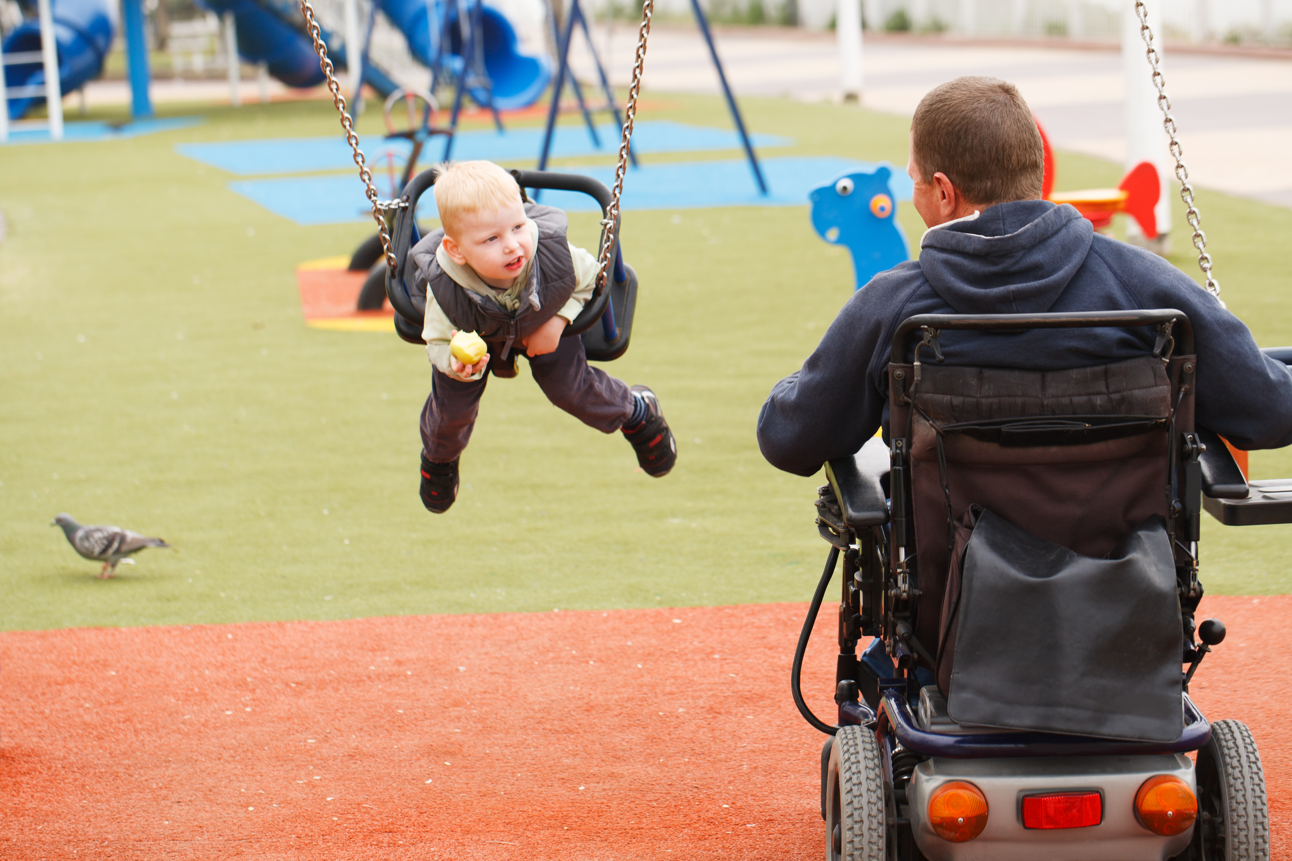 Man in wheelchair pushing his child on the swing
